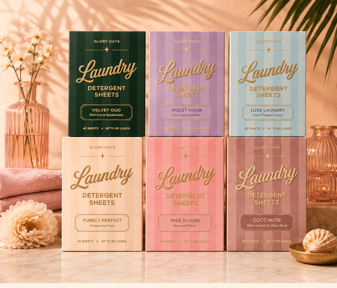 The Glory Days laundry detergent sheet range in six plastic-free striped boxes, styled on marble with flowers and folded towels